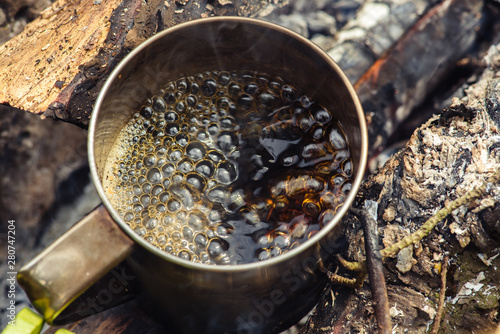 Coffee near the fire outdoors. Adventure, travel, tourism and camping concept. Coffee from mug at camp. Coffee cooked over a campfire on the nature.