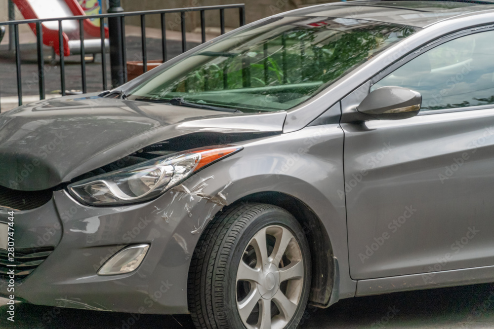 crumpled hood of a gray car after an accident, a part above the wheel is glued with adhesive tape