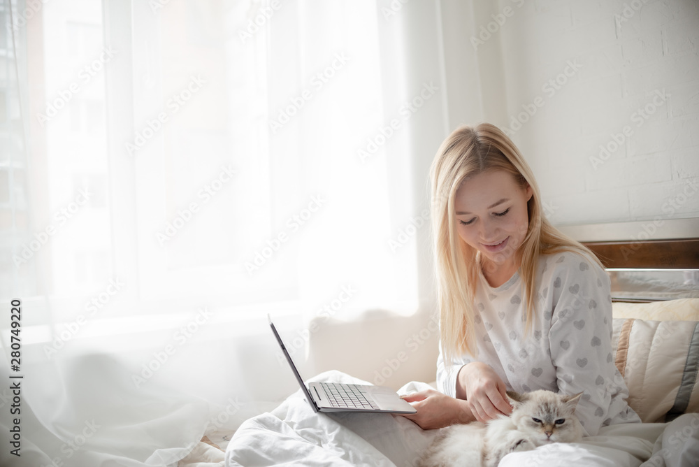 Blonde Giirl typing and using laptop hygge with fluffy cat, pajama and blanket. Hugge and lagom concept comfort and simple life . Horizontal copyspace Blonde Giirl typing and using laptop hygge with fluffy cat, pajama and blanket. Hugge and lagom concept comfort and simple life . Horizontal copyspace