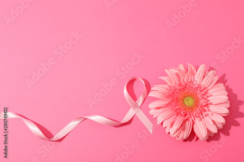 Pink awareness ribbon and gerbera on color background, space for text.