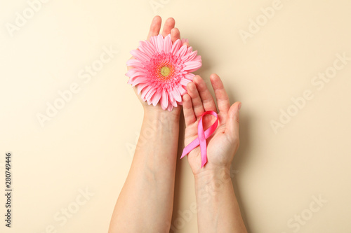 Female hands hold pink awareness ribbon and gerbera on color background