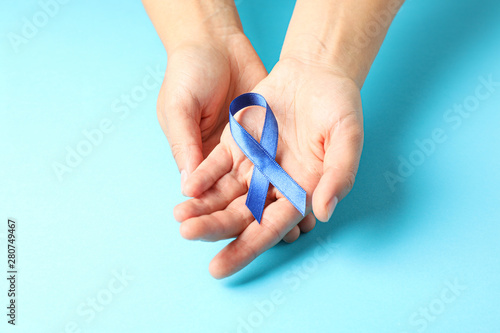 Female hands hold blue awareness ribbon on color background  space for text