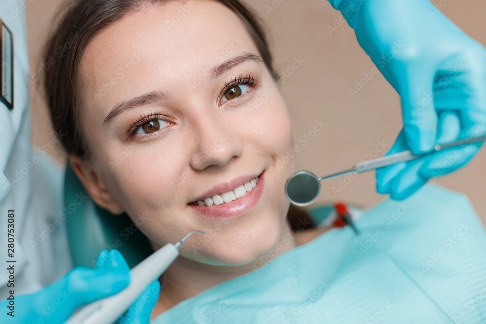 Patient in dental chair. Dentist's hands with blue gloves work with a dental tools. Beautiful young woman having dental treatment at dentist's office. Patient in dental chair. Dentist's hands with blue gloves work with a dental tools. Beautiful young woman having dental treatment at dentist's office.