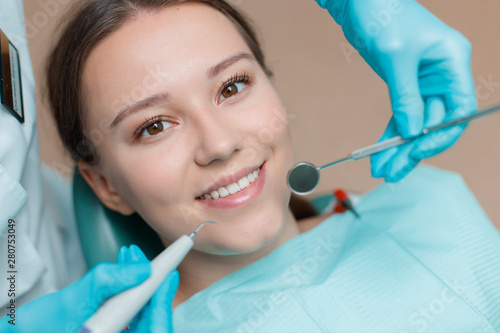 Patient in dental chair. Dentist s hands with blue gloves work with a dental tools. Beautiful young woman having dental treatment at dentist s office.