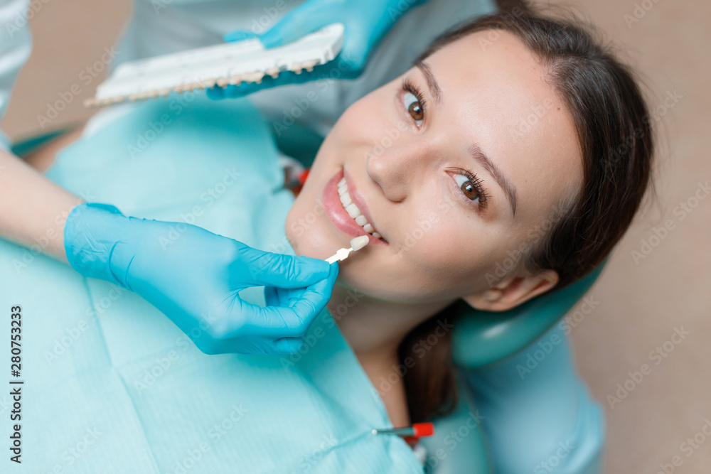 White teeth and beautiful smile of young woman. Matching the shades of the implants using shade guide. Preparation for teeth whitening in dental office. Patient in dental chair. White teeth and beautiful smile of young woman. Matching the shades of the implants using shade guide. Preparation for teeth whitening in dental office. Patient in dental chair.