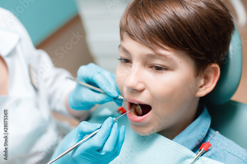 Little boy with open mouth examining dental inspection at dentist office. Dentist s hands with blue gloves work with a dental tools. Healthy teeth concept.