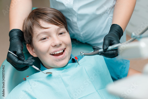 Patient in dental chair. Dentist's hands with black gloves work with a tooth drill and a mirror. Little boy having dental treatment at dentist's office.