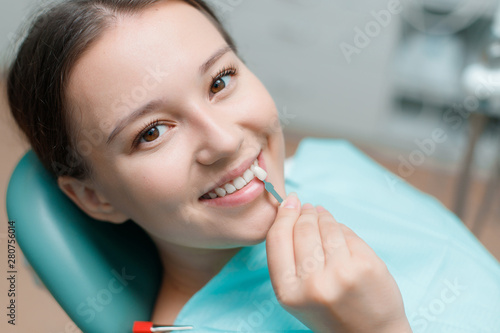 Patient in dental chair. White teeth and beautiful smile of young woman. Matching the shades of the implants using shade guide. Bleaching of the teeth at dentist clinic.