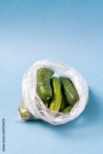 Cucumbers in plastic bag on blue background. Stop using artificial food storage bags concept. photo