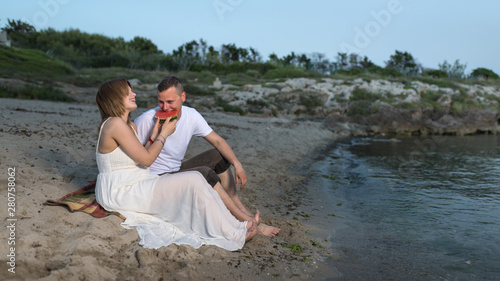 Pregnant couple on the beach, sitting on the sand. Picnic with watermelon.