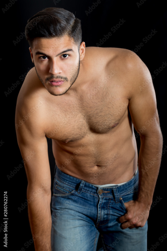 Young latin man poses for a portrait studio shirtless to show off his fitness. 
