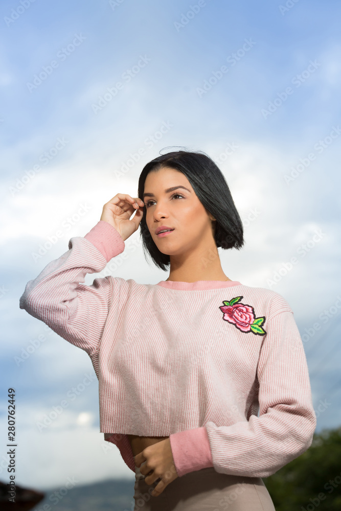 Brunette woman in her 20s in aportrait outdoors. She is smiling and looking to the camera. Her left hand is touching her hair. Brunette woman in her 20s in aportrait outdoors. She is smiling and looking to the camera. Her left hand is touching her hair.