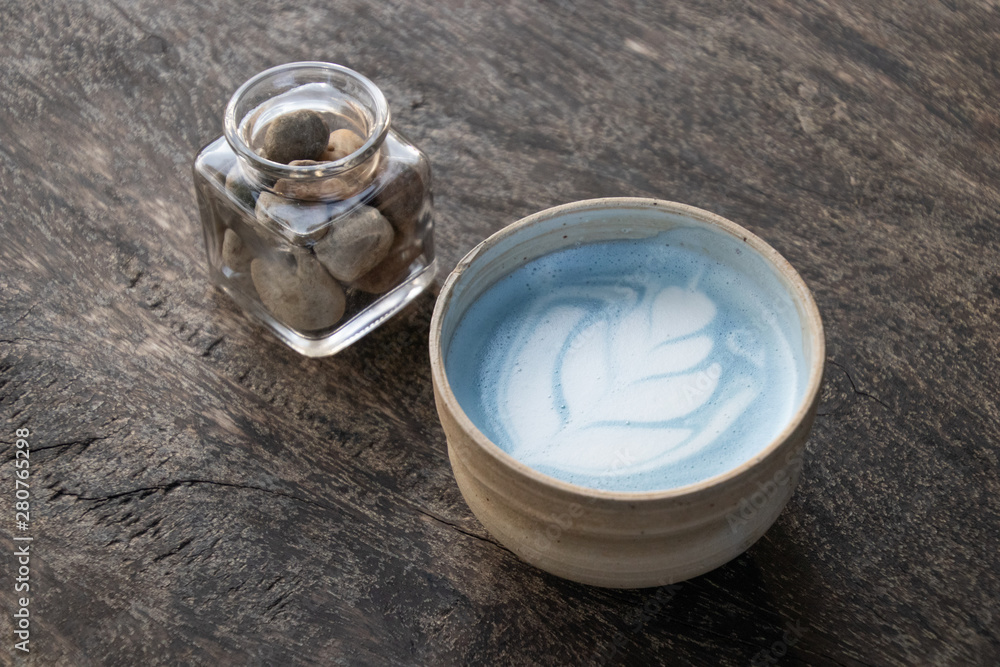 A cup of Blue pea latte coffee with heart shape floaty art.Butterfly pea coffee on wooden table background A cup of Blue pea latte coffee with heart shape floaty art.Butterfly pea coffee on wooden table background