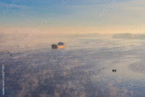 Industrial ship sailing down the river in the mist at morning