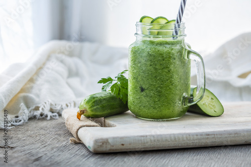 Photo of green cucumber smoothie in jar with straw on light background. Fresh organic Smoothie. Health or detox diet food concept.