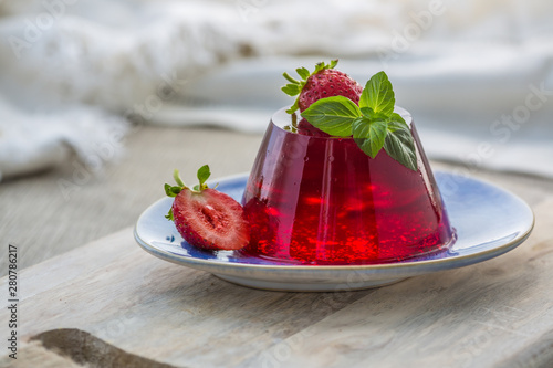 Photo of summer Jelly Dessert with strawberry. Garnished with a sprig of fresh basil on light background.
