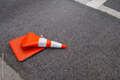 orange and white reflective street cone flat on the tarmac run over by a vehicle/car