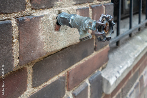 Fotografija outdoor brassy copper faucet on the side of old urban brick building