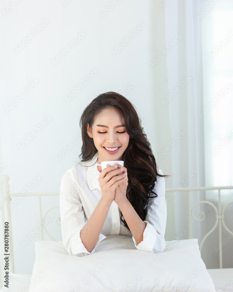 A beautiful asian woman in a white shirt and coffee cup that is smiling happily in the white bed. A beautiful asian woman in a white shirt and coffee cup that is smiling happily in the white bed.