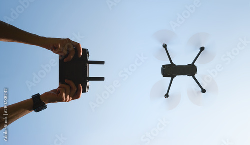 Remote control in men hands and the silhouette of a flying drone. View from the bottom