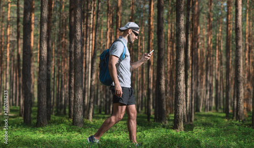 A man walks in the woods and uses a smartphone.