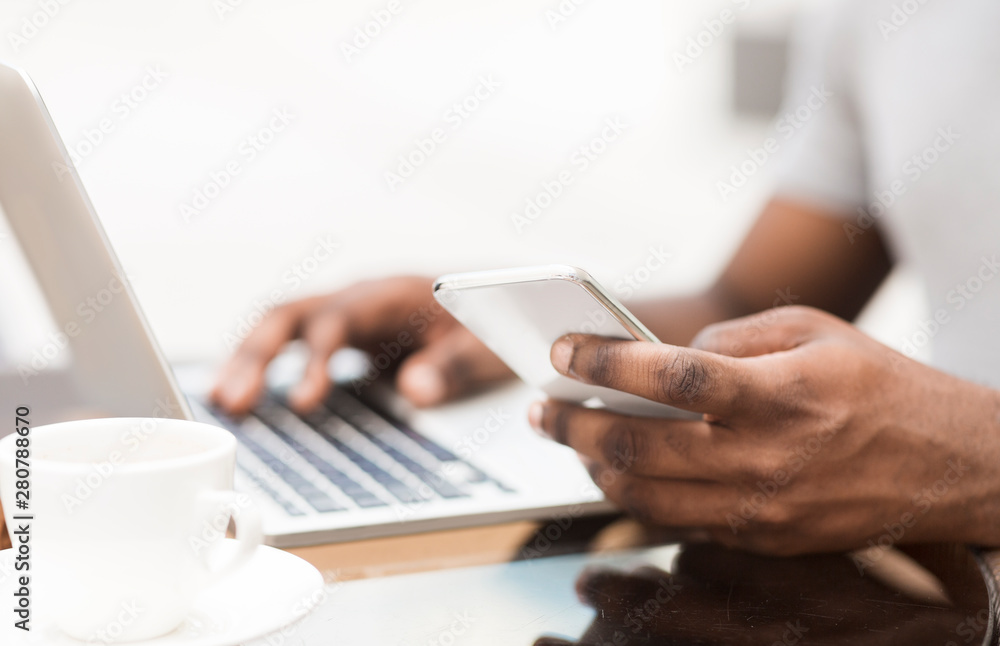 Fototapeta premium Unrecognizable african man using cellphone and laptop