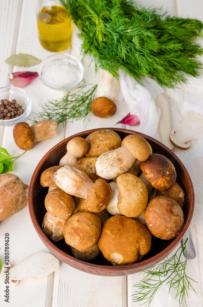 Fresh forest white mushrooms in a bowl with spices and fresh herbs on a wooden background Fresh forest white mushrooms in a bowl with spices and fresh herbs on a wooden background