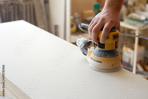 Carpenter grinds the surface of the facade before assembling furniture on a blurred background carpentry workshop, selective focus