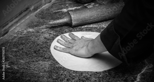 Chef rolling dough for round pizza, closeup