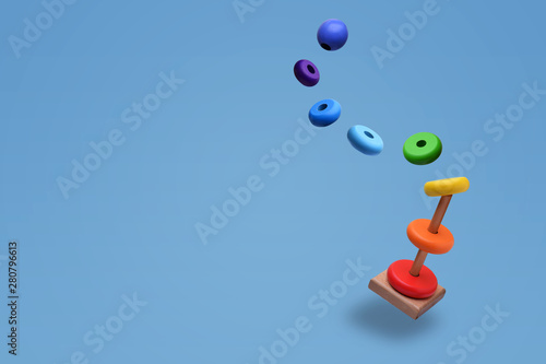 Toy pyramid from rainbow colored wooden rings with a ball head hovers in the air. With flying rings. Toy for babies to joyfully learn mechanical skills and colors. Isolated on light blue background