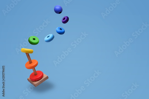 Toy pyramid from rainbow colored wooden rings with a ball head hovers in the air. With flying rings. Toy for babies to joyfully learn mechanical skills and colors. Isolated on light blue background.