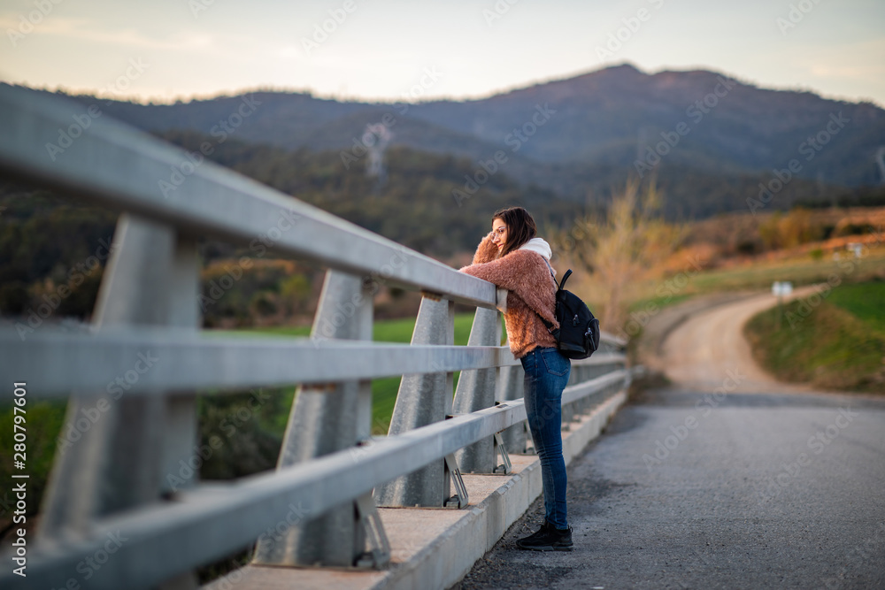 Side shot of a beautiful woman leaning on a metal fence during sunset Side shot of a beautiful woman leaning on a metal fence during sunset