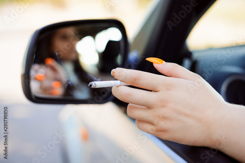 Young girl smoking while driving a car. Female hand with cigarette through the window of a car