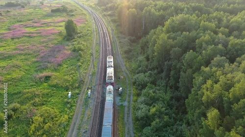 The train goes into the distance in the wild russian forest. Aerial view at sunset. 4k footage from drone