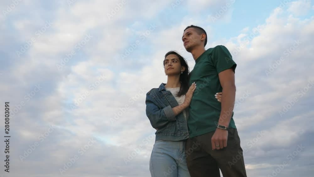 Confident young couple standing and looking forward under fluffy sky in slo-mo Confident young couple standing and looking forward under fluffy sky in slo-mo