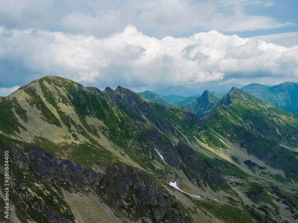 Fototapeta premium View from Banikov peak on Western Tatra mountains or Rohace panorama. Sharp green mountains - ostry rohac, placlive and volovec with hiking trail on ridge. Summer blue sky white clouds.