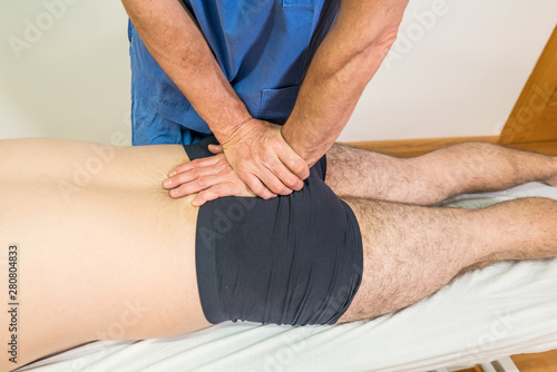 Doctor physiotherapist assisting a male patient while giving exercising treatment massaging the sacrum of patient in a physio room, rehabilitation physiotherapy concept.