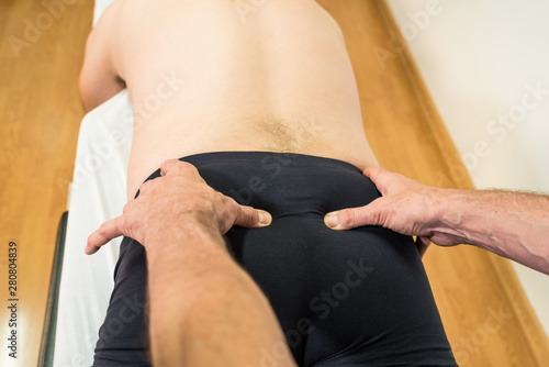 Fotografie Doctor physiotherapist assisting a male patient while giving exercising treatment massaging the sacrum of patient in a physio room, rehabilitation physiotherapy concept