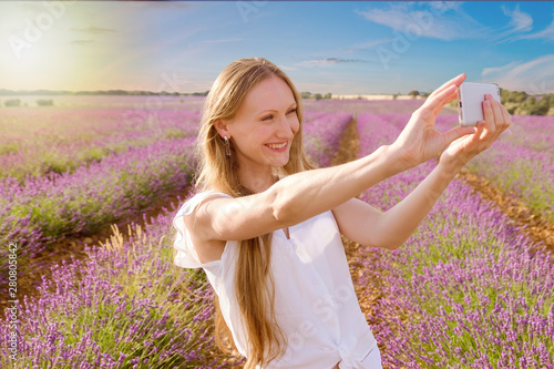 beautiful woman taking a self picture behind purple lavender fields during a summer sunset - Image