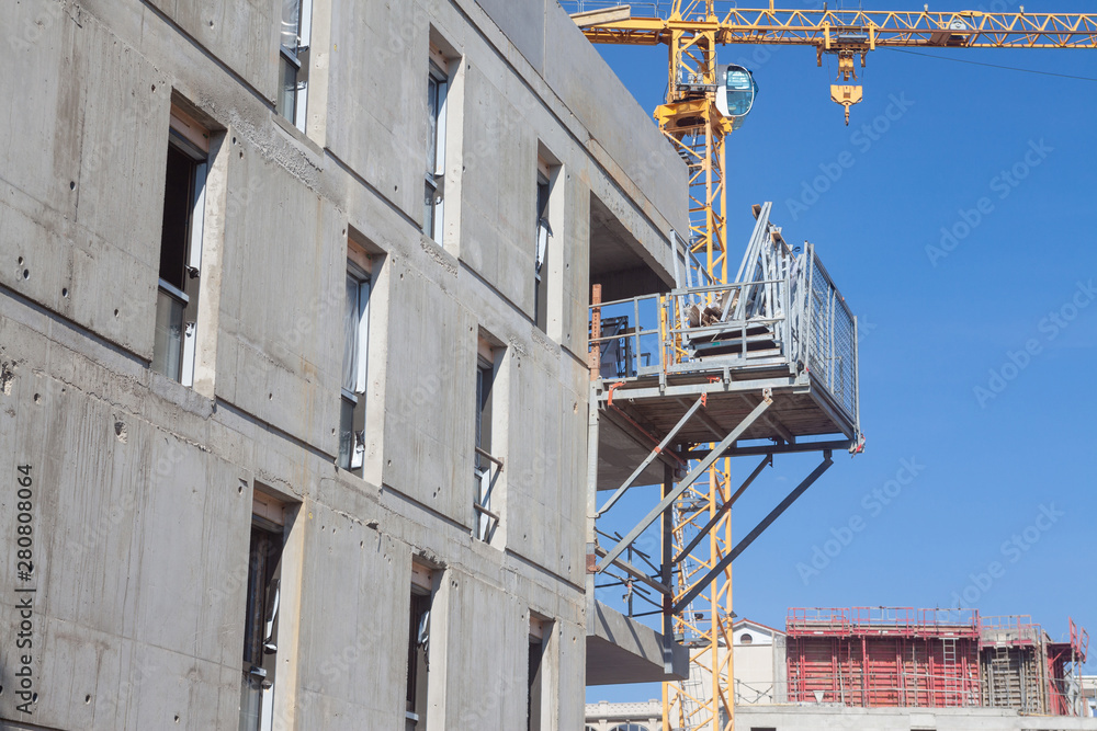 Construction site in France of a residential building, with scaffholdings, concrete facades and cement blocks, as well as cranes visible, in a real estate development area