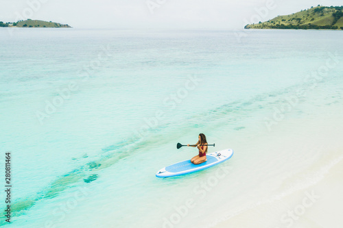 Woman paddling on sup board and enjoying turquoise transparent water and white sand island beach. Tropical travel, wanderlust and water activity concept.