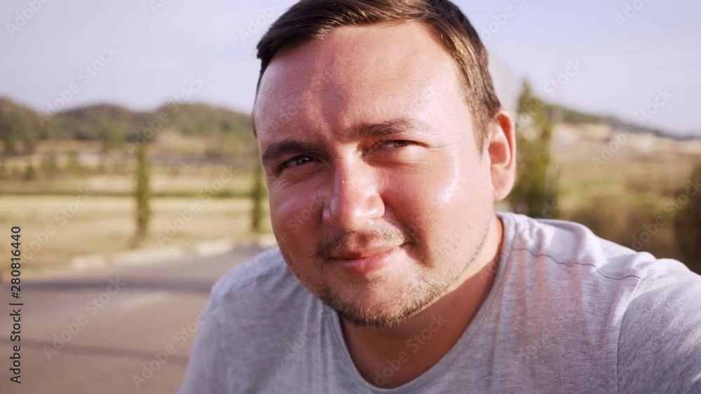 Chubby pleasant man looks in cameo and smiles against the background of the road and trees Chubby pleasant man looks in cameo and smiles against the background of the road and trees