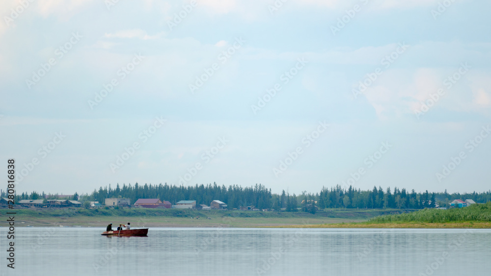 Three vague silhouettes of people of the Northern Yakuts on a boat with oars floating across the river vilyu from shore to shore on the background of village houses Suntar and spruce taiga.
