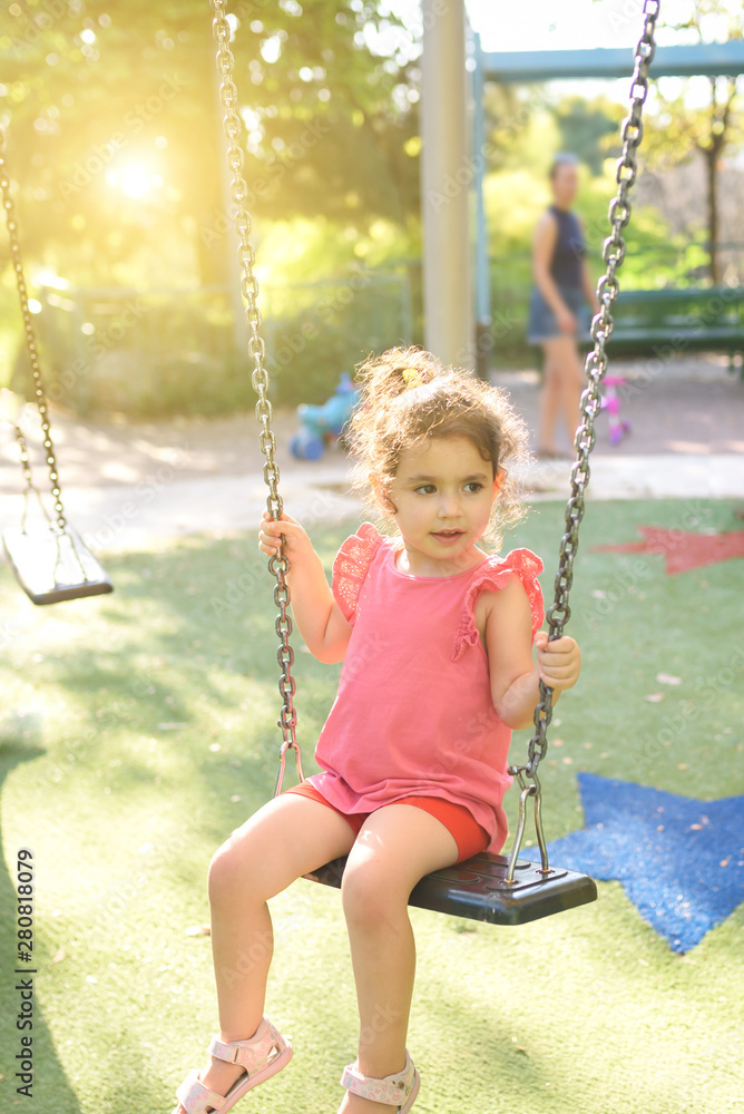 Happy child girl laughing and swinging on a swing at the playground in summer.