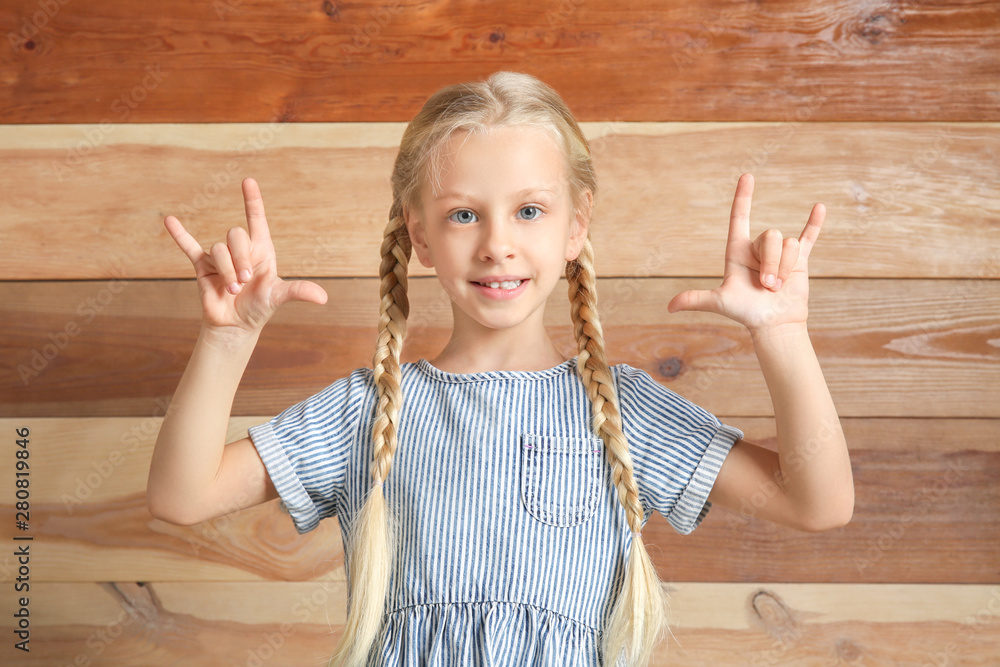 Little deaf mute girl using sign language on wooden background Little deaf mute girl using sign language on wooden background