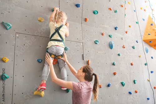 Instructor helping little girl to climb wall in gym