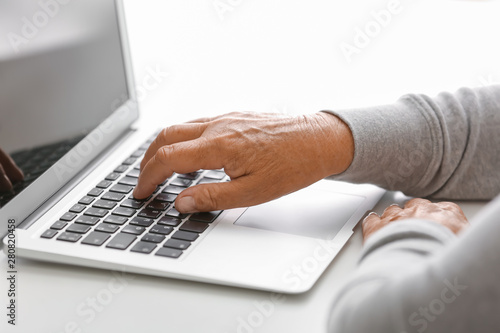 Elderly woman with modern laptop on white table, closeup