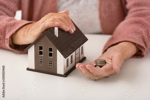 Elderly woman with figure of house and coins, closeup. Concept of payment for utility services