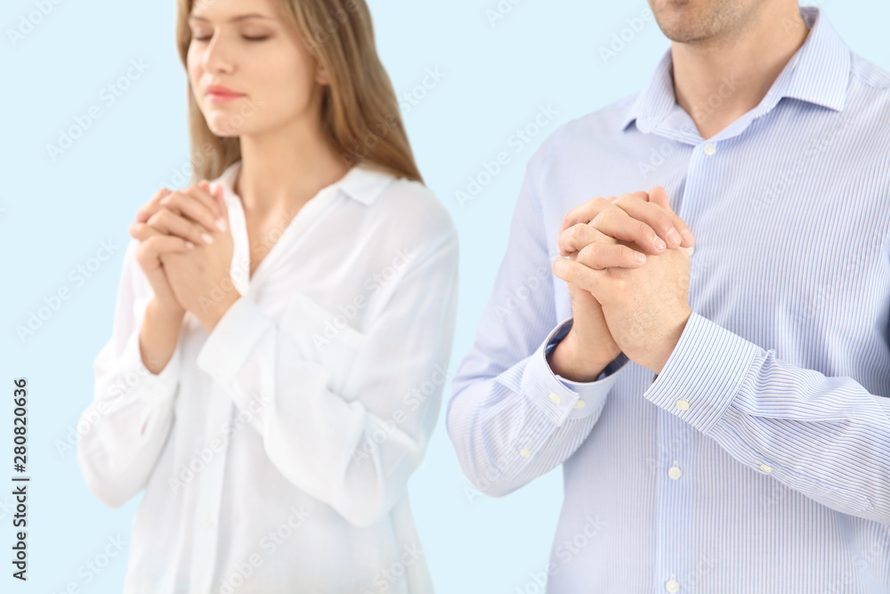 Religious couple praying to God on light color background Religious couple praying to God on light color background