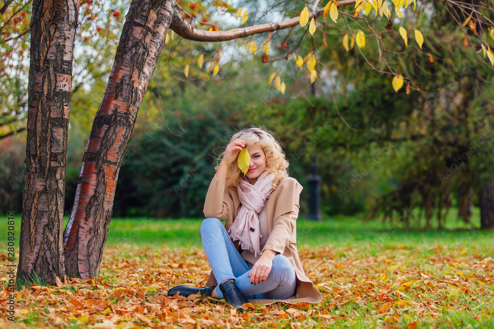 Young beautiful woman sitting on the ground coverd with fallen autumn leaves